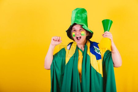 Photo for Adult adult woman, soccer fan from brazil, wearing flag and hat, using horn noise, cheering. - Royalty Free Image