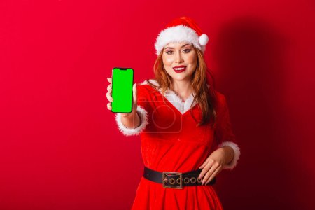Photo for Beautiful Brazilian red-haired woman, dressed in Christmas clothes, Santa Claus. showing smartphone with green chroma screen. - Royalty Free Image