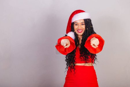 Foto de Mujer negra brasileña, vestida con ropa navideña, feliz Navidad, sonriendo, apuntando a la cámara, eligiéndote. - Imagen libre de derechos