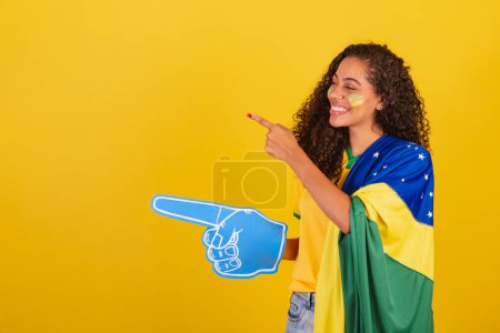 Téléchargez les photos : Jeune Brésilienne noire, fan de foot. avec doigt en mousse pointant vers la gauche. - en image libre de droit