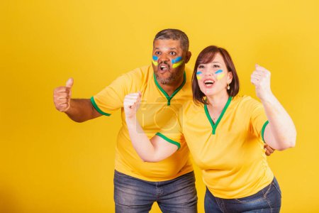 Photo for Couple, red-haired woman and black man, Brazilian soccer fans. celebrating. - Royalty Free Image