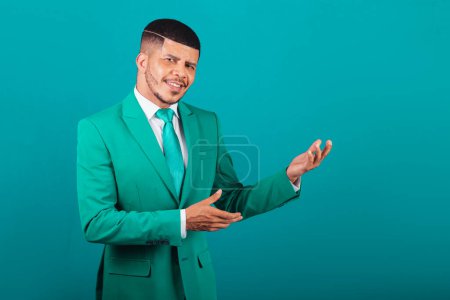 Téléchargez les photos : Homme noir brésilien, vêtu de costume et cravate verte, homme d'affaires. présenter quelque chose à droite - en image libre de droit