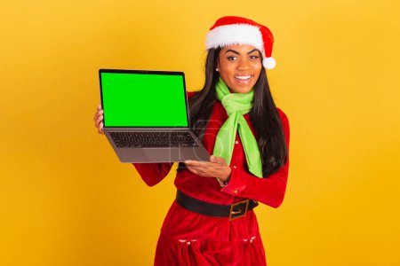 Photo for Beautiful black Brazilian woman, dressed in christmas clothes, santa claus, notebook and showing green chroma screen. - Royalty Free Image