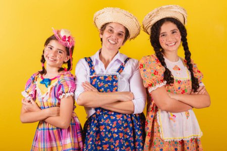 Foto de Abuela y sus dos nietas vestidas con ropa típica de Festa Junina. Brazos cruzados, sonrientes, felices. - Imagen libre de derechos