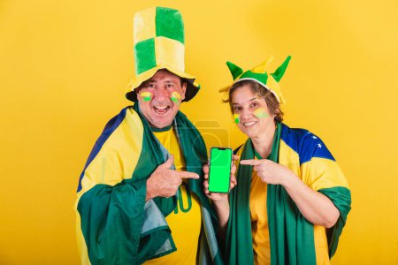 Photo for Adult couple, soccer fan from brazil, using flag. pointing to smartphone screen, app, mobile, advertising photo. - Royalty Free Image