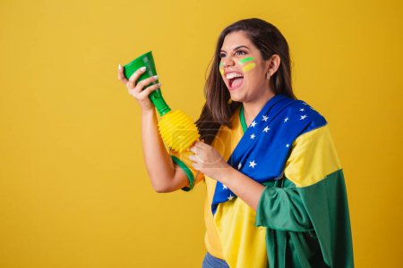 Photo for Woman supporter of Brazil, world cup 2022, soccer championship, using brazil flag as cover. honking and partying at football match. Horn. - Royalty Free Image