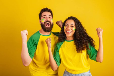 Photo for Couple of brazil soccer supporters, dressed in the colors of the nation, black woman, caucasian man. Twisting and vibrating. - Royalty Free Image