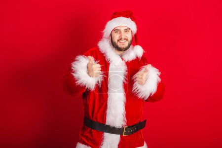 Photo for Caucasian, Brazilian man dressed in Christmas outfit, Santa Claus. Like with your fingers. - Royalty Free Image