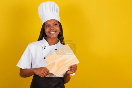 Photo for Young afro brazilian woman, cook, holding wooden board for gastronomy. - Royalty Free Image