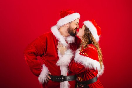 Foto de Pareja brasileña, vestida con ropa de Navidad, Santa Claus, abrazando, dando un beso - Imagen libre de derechos
