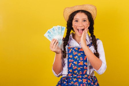 Photo for Girl wearing typical clothes for Festa Junina. Surprised, amazing, wow, unbelievable face holding money bills. - Royalty Free Image