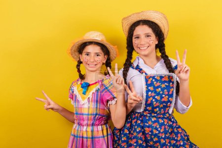 Photo for Sisters and friends, wearing typical clothes of the Festa Junina. Making peace and love sign with fingers. - Royalty Free Image