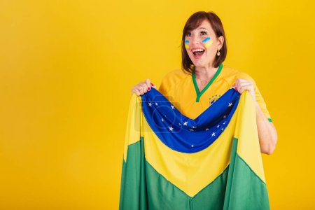 Foto de Mujer pelirroja, fan del fútbol brasileño. ondeando con la bandera de Brasil, animando y celebrando. - Imagen libre de derechos