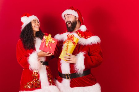 Photo for Brazilian couple, dressed for christmas, santa claus, mummy claus. exchanging gifts. approved, black woman and caucasian man. - Royalty Free Image