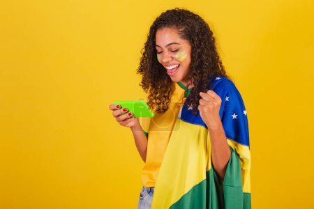 Téléchargez les photos : Jeune Brésilien noir, fan de foot. jeu de jeu, smartphone. - en image libre de droit