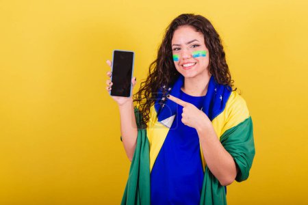 Téléchargez les photos : Femme fan de football, fan de brésil, coupe du monde, tenant le téléphone portable et montrant l'écran. - en image libre de droit