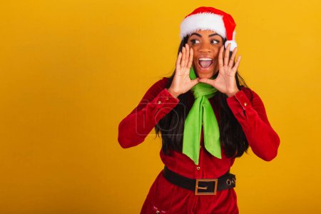 Téléchargez les photos : Belle femme brésilienne noire, vêtue de vêtements de Noël, Santa Claus, criant promotion. - en image libre de droit