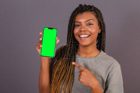Photo for Young afro brazilian woman showing smartphone screen. space for advertisements, applications, mobile. - Royalty Free Image
