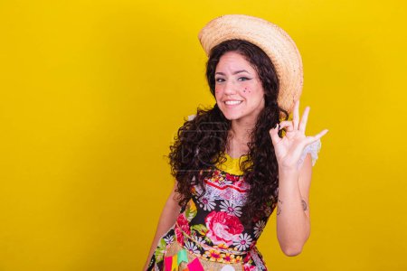 Photo for Beautiful woman dressed in typical clothes for a Festa Junina. Finger ok sign, yes. - Royalty Free Image