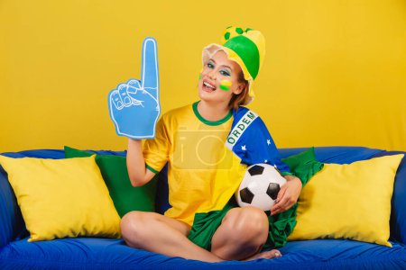 Foto de Caucásico, pelirrojo, brasileño, aficionado al fútbol brasileño en sofá con dedo de espuma y fiesta de pelota - Imagen libre de derechos