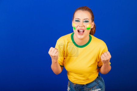 Photo for Caucasian woman, redhead, Brazil soccer fan, Brazilian, blue background, screaming goal - Royalty Free Image