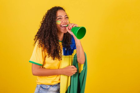Téléchargez les photos : Jeune Brésilienne noire, fan de foot. hurlant à travers haut-parleur. photo publicitaire. - en image libre de droit