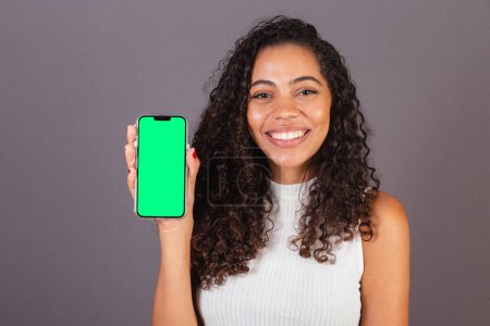 Téléchargez les photos : Jeune femme noire brésilienne tenant un téléphone portable et montrant l'écran, photo publicitaire. - en image libre de droit