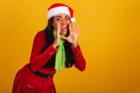 Photo for Beautiful black Brazilian woman, dressed in christmas clothes, santa claus, shouting promotion. - Royalty Free Image