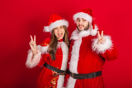 Téléchargez les photos : Couple brésilien avec vêtements de Noël, Père Noël claus. signe de paix et d'amour. - en image libre de droit