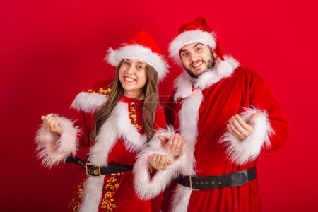 Photo for Brazilian couple with christmas clothes, santa claus. calling with hands, inviting. - Royalty Free Image