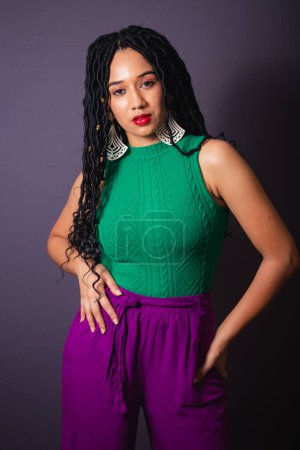 Téléchargez les photos : Belle femme noire brésilienne, vêtue de vert et de violet. Portrait demi-corps, fond infini gris. - en image libre de droit