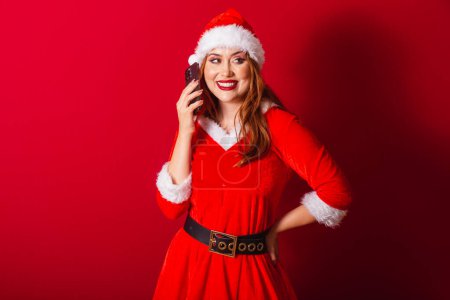 Téléchargez les photos : Belle femme rousse brésilienne, vêtue de vêtements de Noël, le Père Noël. parler sur appel vocal par smartphone. - en image libre de droit