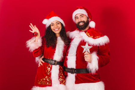 Photo for Brazilian couple, dressed for christmas, santa claus, mummy claus. holding christmas decoration, star, approved, black woman and caucasian man. - Royalty Free Image