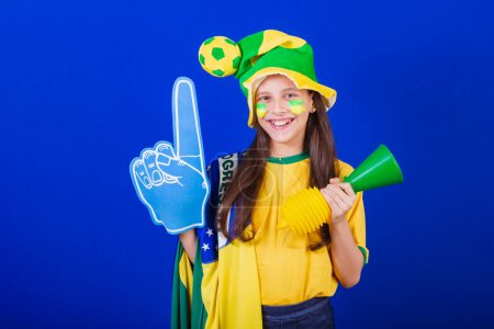 Photo for Young girl, soccer fan from Brazil. dressed in hat and flag. using foam finger - Royalty Free Image