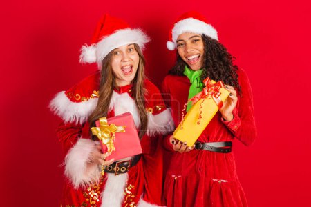 Photo for Two brazilian female friends, dressed in christmas clothes, santa claus, holding christmas gifts. - Royalty Free Image