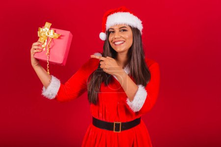 Photo for Beautiful Brazilian woman dressed in Christmas clothes, Santa Claus. showing red gift. - Royalty Free Image