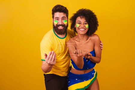 Photo for Couple of brazilian soccer fans, dressed in the colors of brazil, black woman, caucasian man. inviting hands. calling, welcome - Royalty Free Image