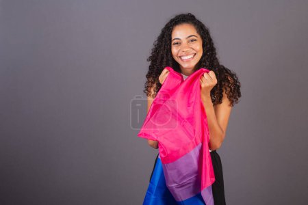 Téléchargez les photos : Jeune femme brésilienne noire tenant un drapeau bisexuel et souriant regardant la caméra, Femme bisexuelle, LGBT, LGBTQ - en image libre de droit