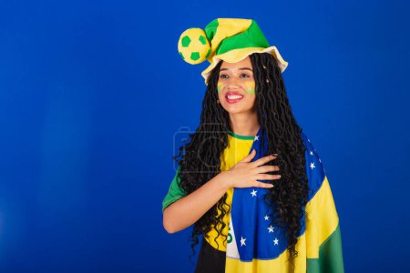 Photo for Young black Brazilian woman, soccer fan. with brazil flag. with hand on chest, gratitude. - Royalty Free Image