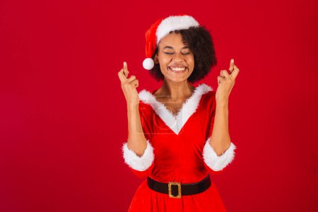Téléchargez les photos : Belle femme brésilienne noire, habillée en Père Noël claus, maman claus, doigts croisés, souhaitant, acclamant, voulant - en image libre de droit