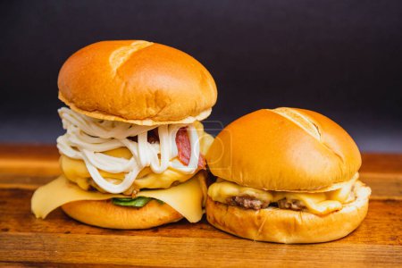 Foto de Deliciosa hamburguesa de res triple hecha a mano con queso cuajada, mozzarella y tocino frito. al lado de x hamburguesa de queso, carne de queso en tablero de madera. - Imagen libre de derechos