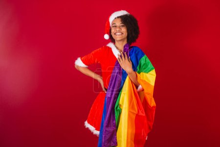 Photo for Beautiful black brazilian woman, dressed as santa claus, mama claus, with flag lgbt diversity, gays and lesbians - Royalty Free Image