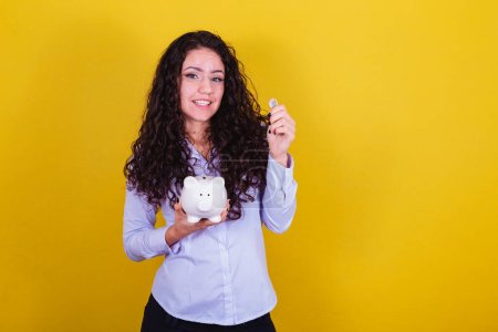 Photo for Caucasian, brazilian woman holding coin and piggy bank, concept of finance, economy, saving. - Royalty Free Image