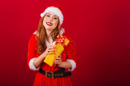 Photo for Beautiful Brazilian red-haired woman, dressed in Christmas clothes, Santa Claus. holding yellow gift. - Royalty Free Image