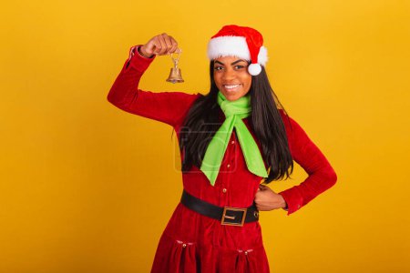 Téléchargez les photos : Belle femme brésilienne noire, vêtue de vêtements de Noël, Père Noël claus, tenant cloche de Noël. - en image libre de droit