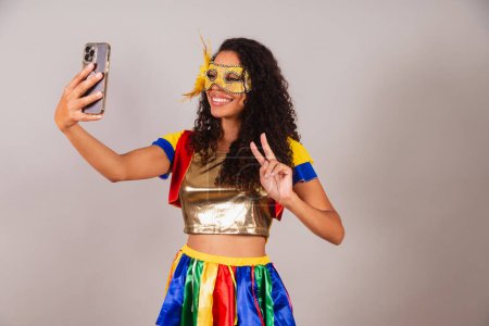 Photo for Beautiful black Brazilian woman, wearing carnival clothes, taking selfie with smartphone. - Royalty Free Image