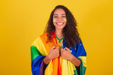 Foto de Joven brasileña negra, fanática del fútbol. con la bandera LGBT y brasileña, Luchar contra los prejuicios. Sonriendo. - Imagen libre de derechos