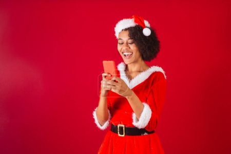 Téléchargez les photos : Belle femme brésilienne noire, habillée en Père Noël claus, maman claus, regarder quelque chose sur smartphone - en image libre de droit