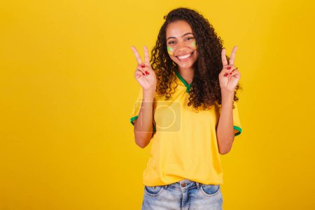 Photo for Young black Brazilian woman, soccer fan. peace and love sign with fingers, good vibes - Royalty Free Image