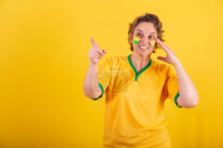 Foto de Mujer adulta adulta, aficionado al fútbol brasileño, apuntando algo a la distancia, foto publicitaria. - Imagen libre de derechos